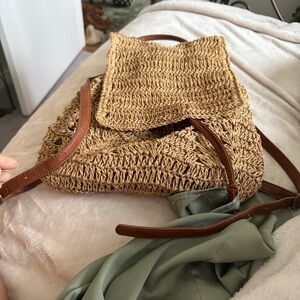 a woven straw backpack with a drawstring closure and brown faux leather straps